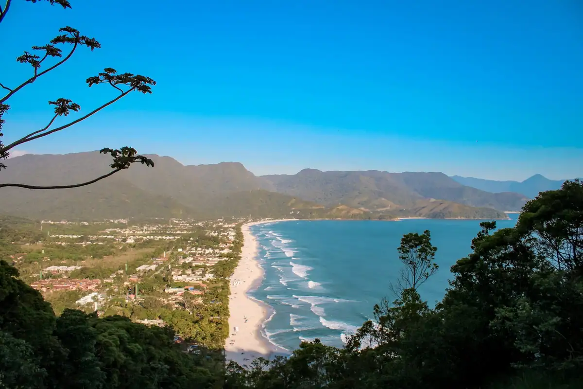 Vista do alto da praia de Maresias, com a faixa de areia entre o mar azul e os morros verdes